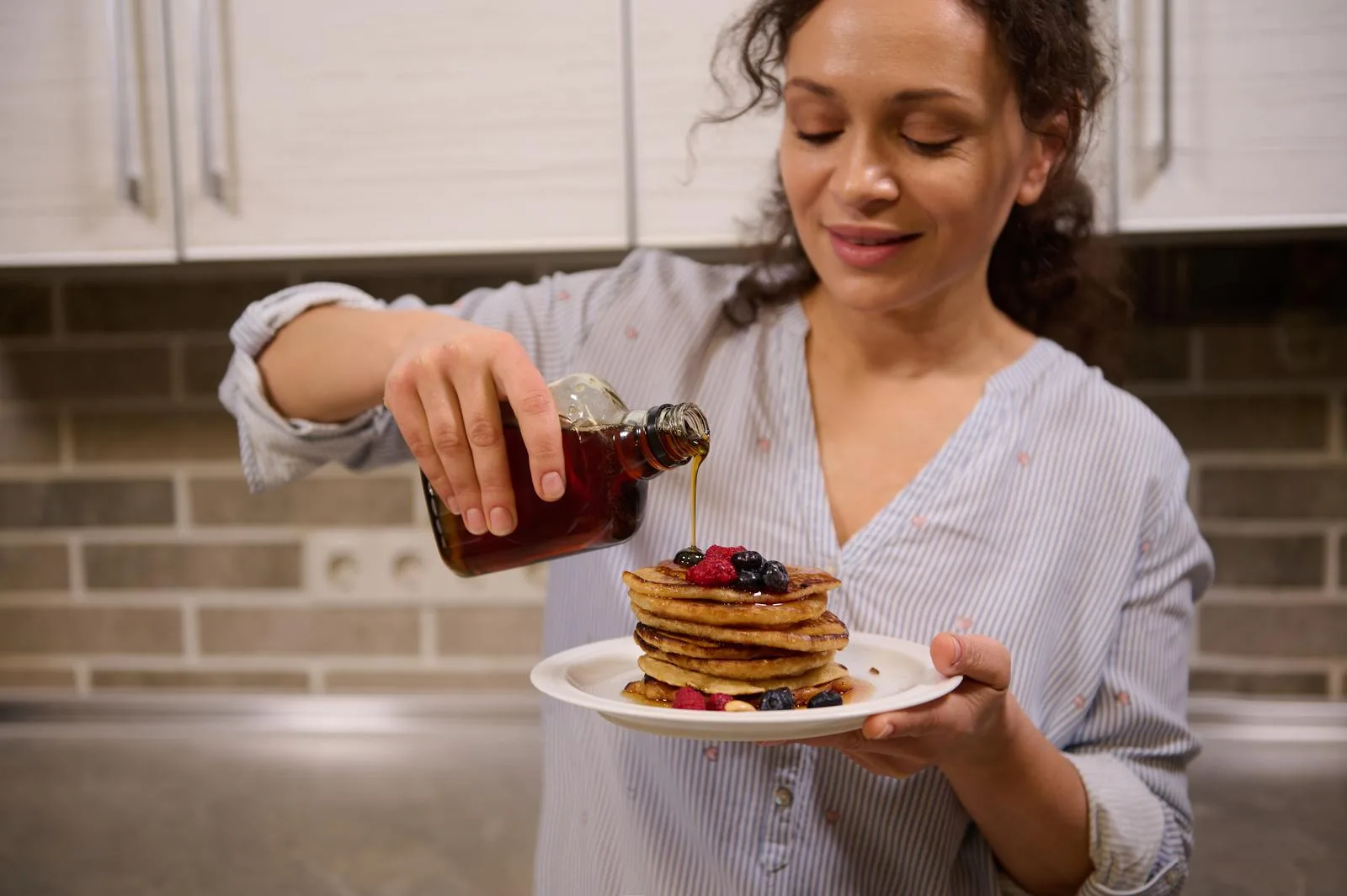 A pretty woman pouring maple syrup on a stack of homemade pancakes